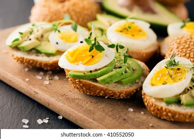 Summer avocado sandwich on bagel with boiled eggs and fresh thyme on stone black background, selective focus - Powered by Shutterstock