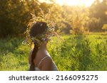 Summer background. Girl in flower wreath on meadow, sunny background. Floral crown, symbol of Midsummer, summer solstice, wiccan Litha, Ivan Kupala holiday. Rustic landscape with woman