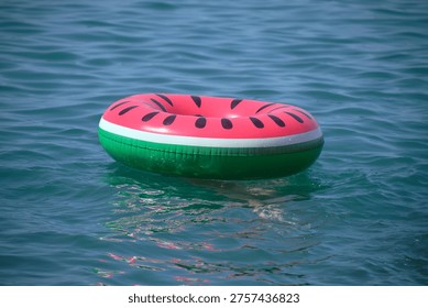 Summer background, relaxation. An inflatable float ring with watermelon image floats in sea or river. Toy for water and beach. lifeguard. Not AI.