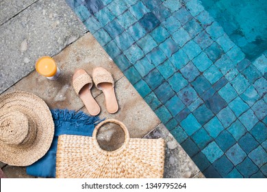 Summer background with straw hat, flip flops, wicker bag, blue  pareo and orange fresh juice near the swimming pool. Summer holiday trendy concept. Top view.