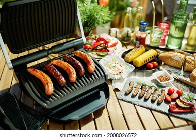 Summer Backyard Picnic. Desk With Electric Grill And Grilled Sausages.