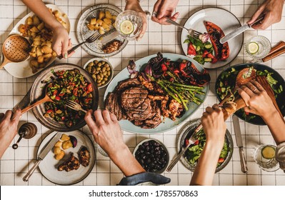 Summer Barbeque Party. Flat-lay Of Table With Grilled Meat, Vegetables, Salads, Roasted Potato And Peoples Hands Over White Tablecloth, Top View. Family Gathering, Feasting, Comfort Food Concept