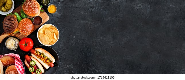 Summer BBQ food side border with hot dog and hamburger buffet. Top down table scene over a dark slate background. Copy space.