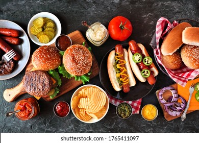 Summer BBQ Food Table With Hot Dog And Hamburger Buffet. Top Down View Over A Dark Slate Background.