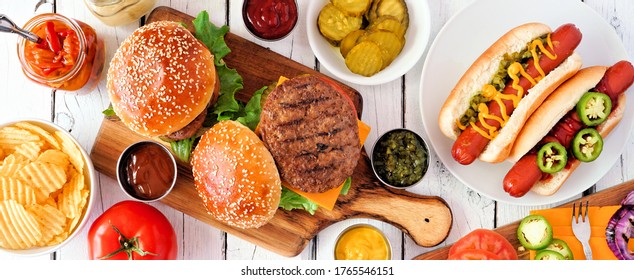 Summer BBQ Food Table Scene With Hot Dog And Hamburger Buffet. Top Down View Banner Over A White Wood Background.