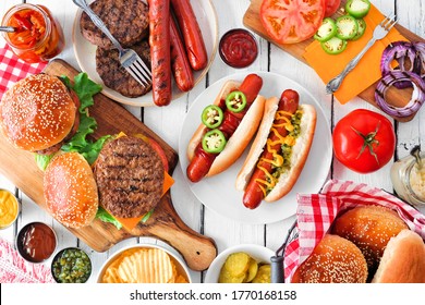 Summer BBQ Food Table Scene With Hot Dog And Hamburger Buffet. Overhead View On A White Wood Background.