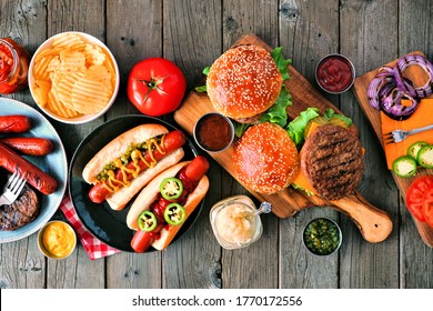 Summer BBQ food table scene with hot dog and hamburger buffet. Above view over a rustic wood background.