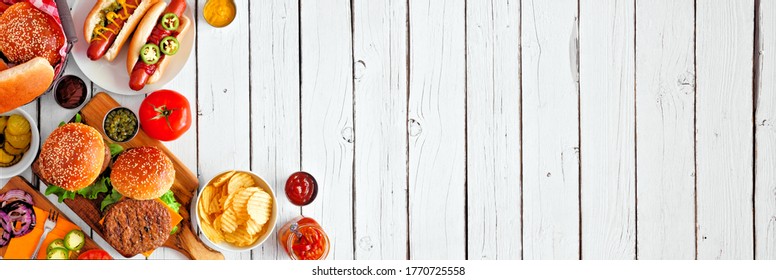 Summer BBQ Food Table Scene With Hot Dog And Hamburger Buffet. Above View Corner Border Over A White Wood Banner Background. Copy Space.