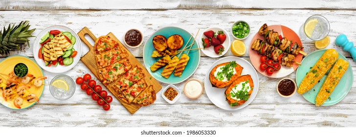 Summer BBQ Grill Table Scene Over A White Wood Banner Background. Grilled Flatbread, Chicken And Shrimp Skewers, Stuffed Sweet Potato, Corn, Fruit And Salad. Overhead View.