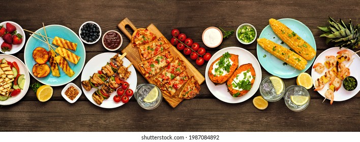 Summer BBQ Grill Table Scene Over A Dark Wood Banner Background. Grilled Flatbread, Chicken And Shrimp Skewers, Stuffed Sweet Potato, Corn, Fruit And Salad. Above View.