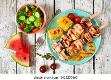 Summer BBQ Or Picnic Food Concept. Salad, Grilled Kabobs, Corn And Fruit. Top View Table Scene Over A White Wood Background.