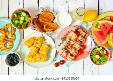 Summer BBQ Or Picnic Food Concept. Selection Of Fruits, Salad, Grilled Meat And Potatoes. Top View Table Scene Over A White Wood Background.