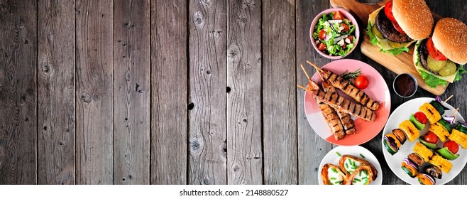 Summer BBQ or picnic food side border. Selection of burgers, grilled meat, vegetables, fruits, salad and potatoes. Overhead view on a dark wood banner background. Copy space. - Powered by Shutterstock