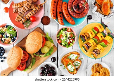 Summer BBQ Or Picnic Food Table Scene. Assortment Of Burgers, Grilled Meat, Vegetables, Fruits, Salad And Potatoes. Overhead View On A White Wood Background.