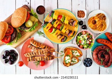 Summer BBQ Or Picnic Food Table Scene. Selection Of Burgers, Grilled Meat, Vegetables, Fruits, Salad And Potatoes. Overhead View On A White Wood Background.