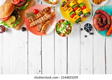 Summer BBQ Or Picnic Food Top Border. Variety Of Burgers, Grilled Meat, Vegetables, Fruits, Salad And Potatoes. Overhead View On A White Wood Background. Copy Space.