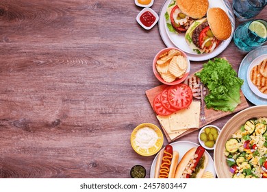 Summer BBQ or picnic side border with hamburgers, hotdogs, salad and snacks. Above view over a dark wood background. Copy space. - Powered by Shutterstock