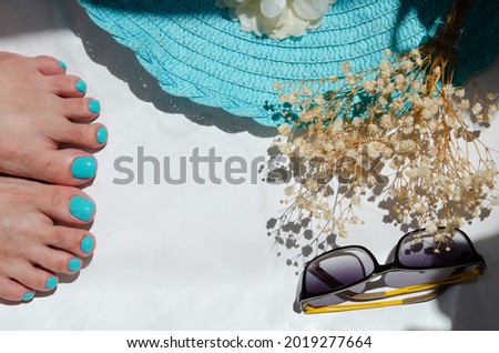 Summer beach concept with female legs. Turquoise nail polish. Nice pedicure fingers, straw hat, sunglasses, gypsophila flowers. Health and body care. Place for your text.