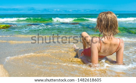 Summer beach concept. Girl tourist in a bathing suit, summer hot day is lying on the sandy beach of the sea. A foamy wave washes her feet, forming beautiful splashes.