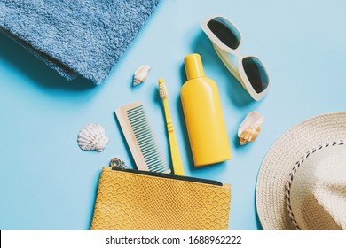 Summer beach essentials. Blue cotton towel, yellow cosmetic bag, wooden comb, toothbrush, sunscreen lotion, sunglasses, wicker hat and seashells on a blue background. Flat lay photography - Powered by Shutterstock