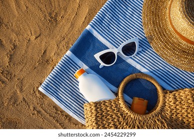 Summer beach essentials laid on sand for sun protection. Straw hat, white sunglasses, sunscreen bottle, and woven bag ready for day by sea. Holiday accessories for UV defense on sunny ocean shore. - Powered by Shutterstock