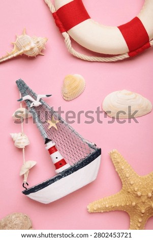 Summer beach flat lay featuring straw sun hat, black sunglasses, seashells, starfish, decorative sailboat and lighthouse accent on pink background. Vertical photo