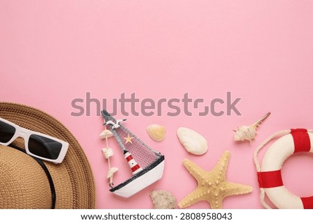 Summer beach flat lay featuring straw sun hat, black sunglasses, seashells, starfish, decorative sailboat and lighthouse accent on pink background. Space for text