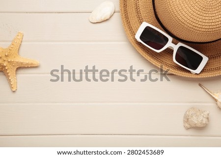 Summer beach flat lay. Straw sun hat, black sunglasses, seashells, starfish on light wooden background. Space for text