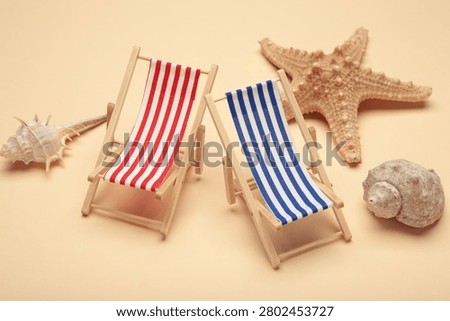Summer beach flat lay. Two miniature deck chairs with seashells, starfish on beige background. Top view
