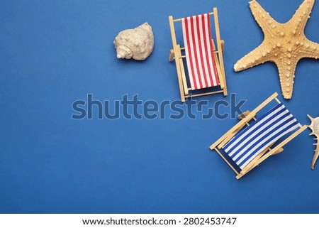 Summer beach flat lay. Two miniature deck chairs with seashells, starfish on dark blue background. Top view