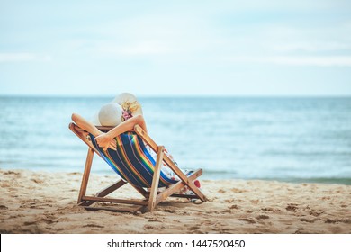 Summer beach travel vacation concept, Traveler asian woman with hat and dress relax on chair beach at Pattaya, Chon Buri, Thailand