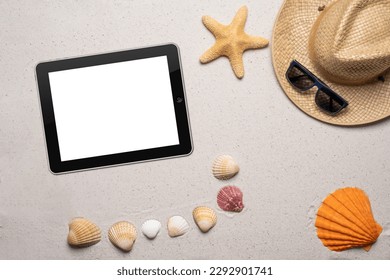 Summer, beach and vacation concept with free text space. Top view. Blank tablet, sun glasses, a man straw hat and orange scallop shell and other small shells on a fine sandy background