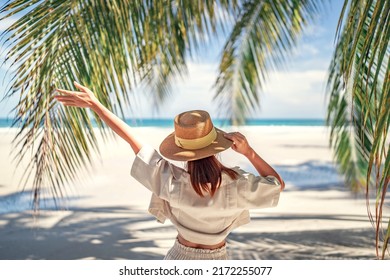 Summer beach vacation concept, Happy woman with hat relaxing at the seaside and looking away, in the summer against a backdrop of palm trees and sea beach.
