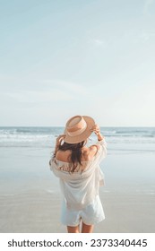 Summer beach vacation concept, Young woman with hat relaxing with her arms raised to her head enjoying looking view of beach ocean on hot summer day.