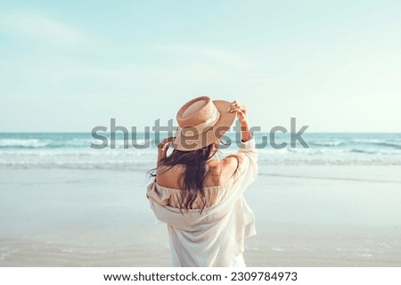 Summer beach vacation concept, Young woman with hat relaxing with her arms raised to her head enjoying looking view of beach ocean on hot summer day, copy space.