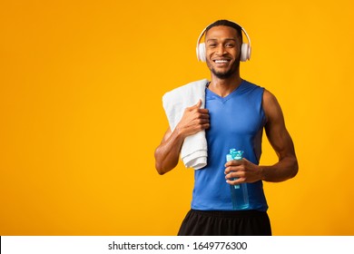 Summer Body. Smiling Black Man Wearing Headphone, Holding Towel And Water Bottle Looking At Camera, Copyspace