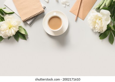 Summer breakfast with coffee cup, sketchbook for planning and white peonies flowers on gray office desk. View from above, flat lay.