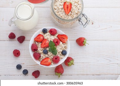 Summer breakfast. Ingredients for healthy breakfast - berries, fruit and muesli on white wooden table, close-up top view horizontal.
