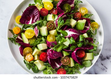 summer bright fresh salad of cherry tomatoes, avocado and radicchio leaves on a white marble table. concept of healthy eating. 