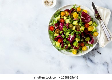 summer bright fresh salad of cherry tomatoes, avocado and radicchio leaves on a white marble table. concept of healthy eating. copy space - Shutterstock ID 1038985648