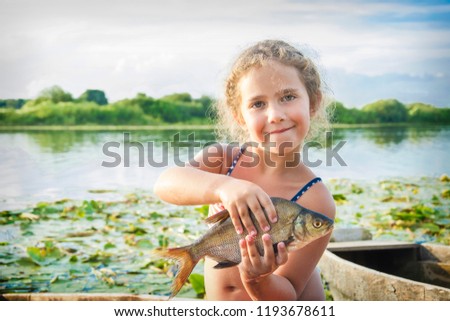 In the summer of bright sunny day a little happy girl on the river caught a big bream.