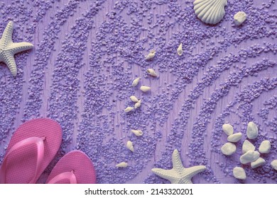 Summer by the sea. Magenta rubber flip-flops, slippers on pebbles with starfish, sea shells and pebbles, studio concept. Purple textured monochromatic background.