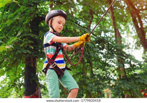 Summer camp. Boy passing the\
cable route high among trees. Climbing the rope park. Summer sunny\
day. Rope playground structure. Safe climbing extreme\
sport.