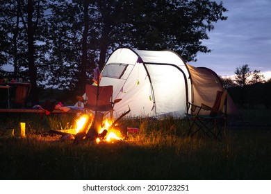 Summer camping. Traveling with a tent. Campfire sunset. Different things and folding chairs near the tent. - Shutterstock ID 2010723251