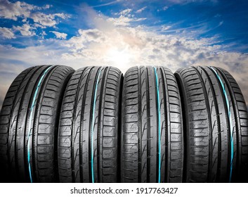 Summer car tires on over blue sky with clouds. Tire stack background. Car tyre protector close up. Black rubber tire. Brand new car tires. Close up black tyre profile. Car tires in a row