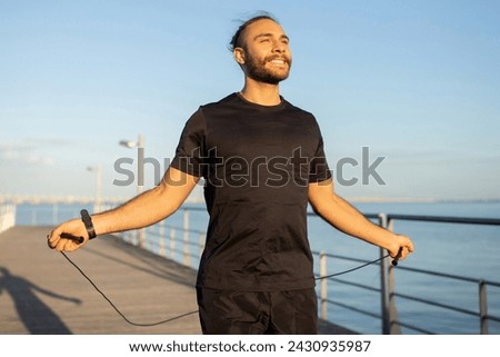 Summer Cardio Workout. Active athletic man skips rope on a seaside pier working out outdoor, promoting fitness motivation and healthy sporty lifestyle, looking aside with smile