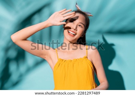 summer casual freshness asian woman yellow summer dress hand rise up to protect sun light shine above,asia woman confident smiling standing studio shot on blue colour background summer concept
