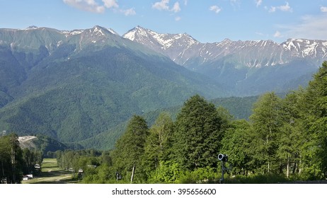 Summer in the Caucasian mountains, green trees and snow-capped peaks, ski resort Rosa Khutor, Russia