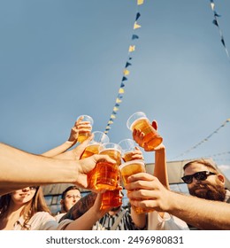 Summer celebration, friends clink beer glasses under a bright blue sky. Young positive people, men and women meeting outdoors on festival. Concept of summer, leisure, friendship, meeting, relaxation - Powered by Shutterstock