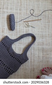 Summer Chain Stitch Handcrafted Bag And A Crochet Yarn Over A Burlap Background Next To A Pair Of Woman Naked Feet.